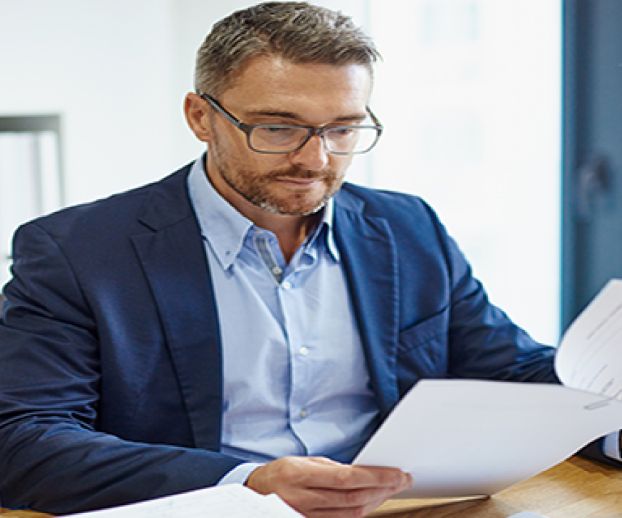 Business man in glasses reviewing printed report output in office setting.