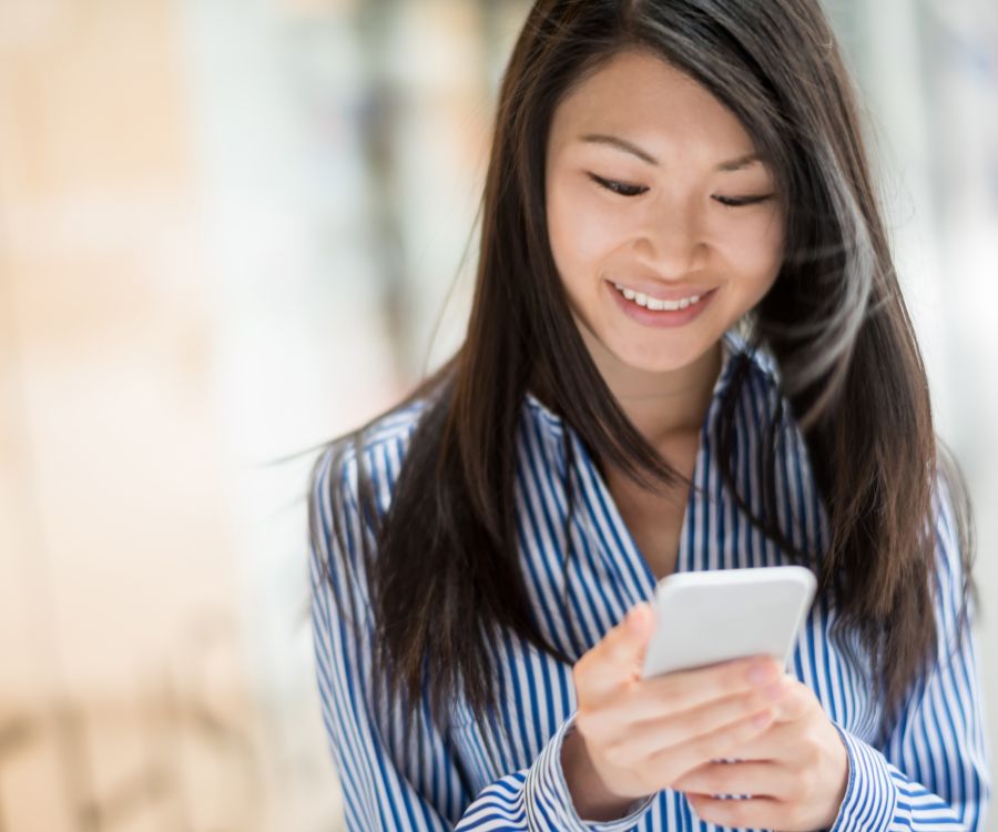 Woman indoors smiling as she uses her mobile phone