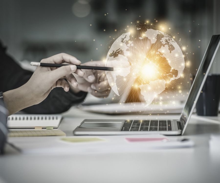 Two people working together at a desk, with a glowing globe hovering above their laptop. 