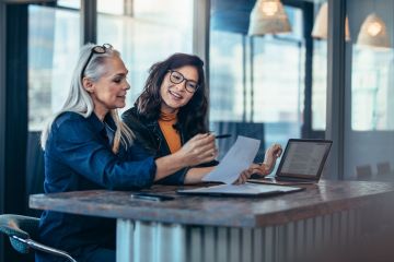 An older woman collaborating with a younger woman over paperwork.