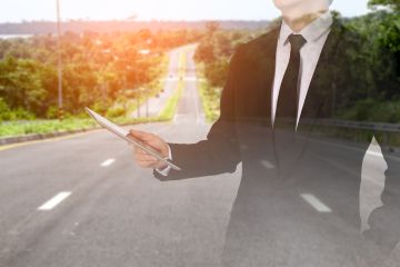 Businessman holding pointer superimposed over open highway and countryside