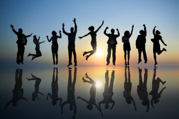 Jumping people silhouetted against a sunset on a shiny floor, like wet sand.