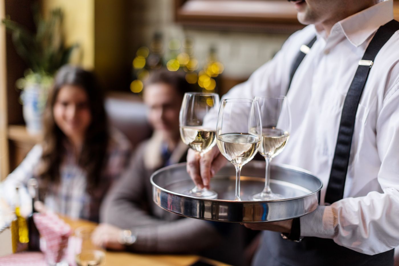 Well-dressed waiting serving glasses of white wine to two guests.