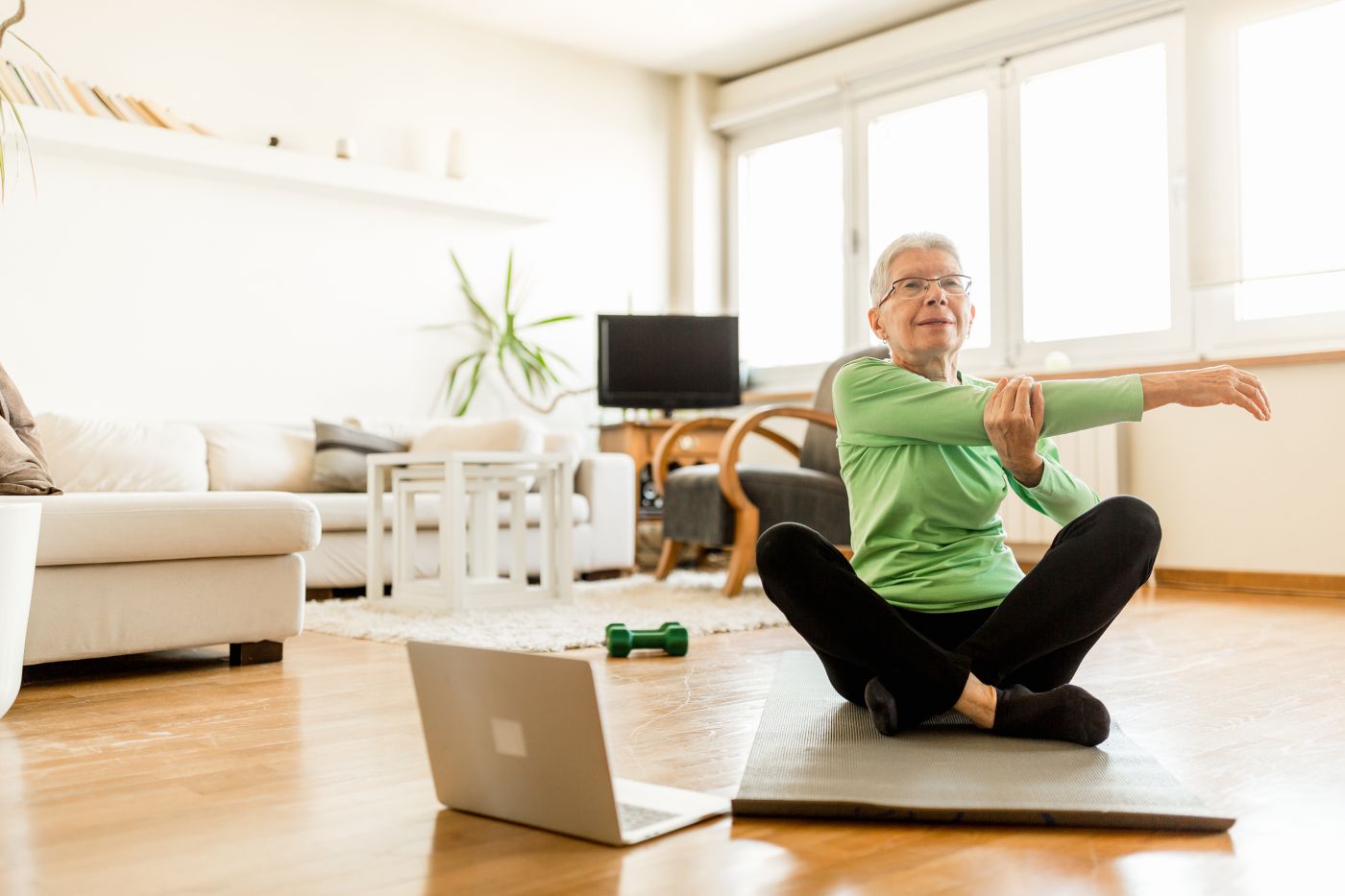 A fit, short-haired elderly lady stretching and exercising on a yoga mat.